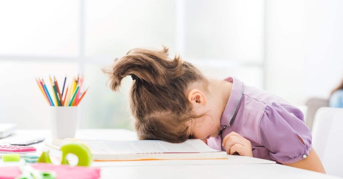 kid doing homework with their head down on the desk