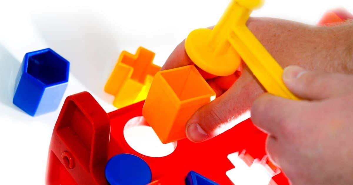 person holding a plastic toy hammer trying to fit a square peg into a round hole