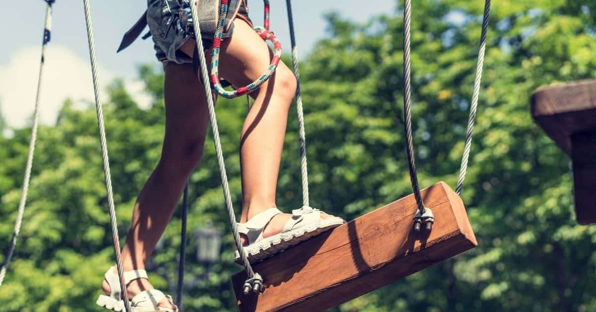 photo of a person in a harness walking across suspended steps of a ropes course