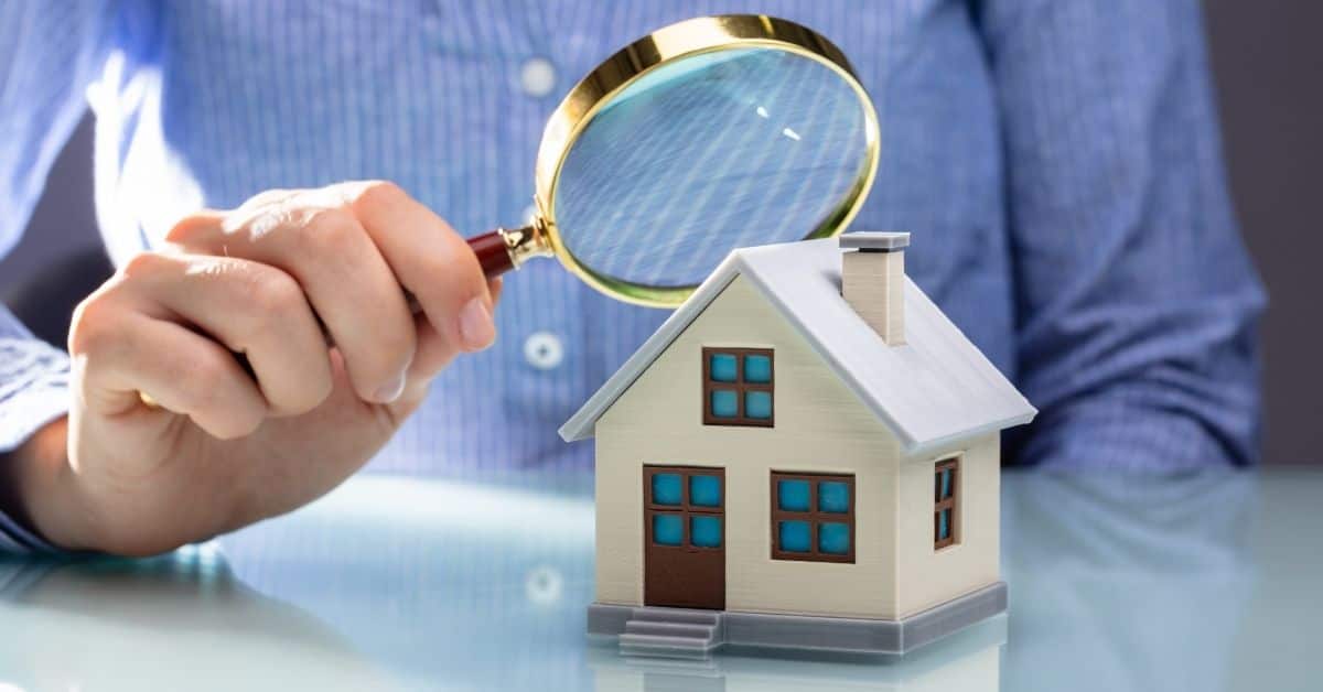 person holding a magnifying glass over a small model of a house